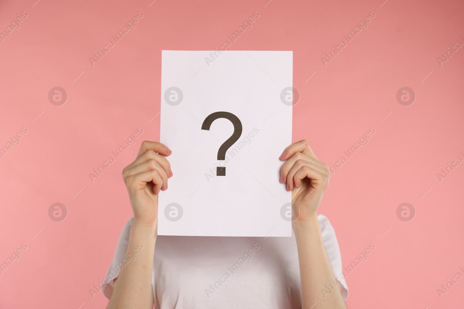 Anonymity. Woman hiding behind paper sheet with question mark on pink background Photo of Anonymity. Woman hiding behind paper sheet with question mark on pink background
