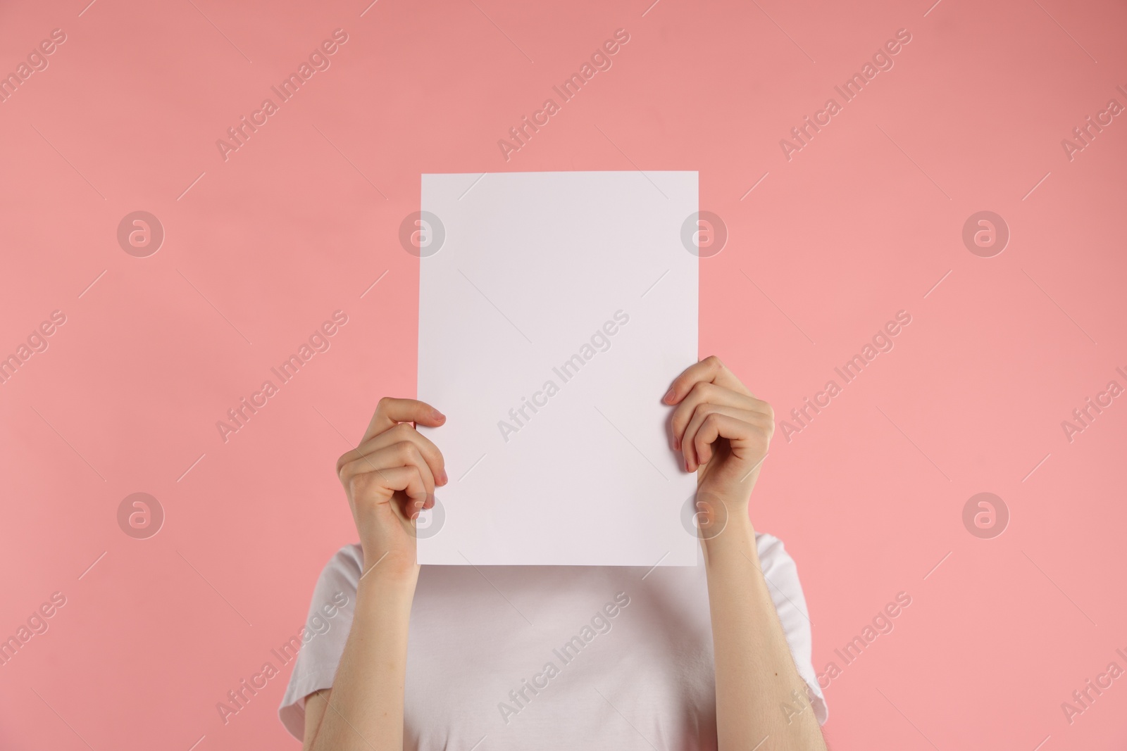 Anonymity. Woman hiding behind blank paper sheet on pink background Photo of Anonymity. Woman hiding behind blank paper sheet on pink background