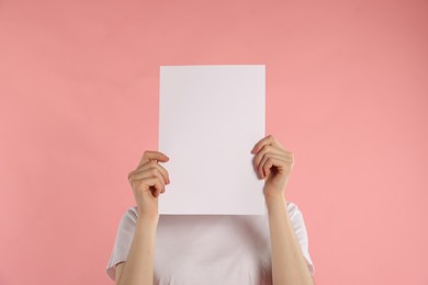 Photo of Anonymity. Woman hiding behind blank paper sheet on pink background