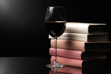 Photo of Red wine in glass and stack of books on mirror table against black background, closeup. Space for text