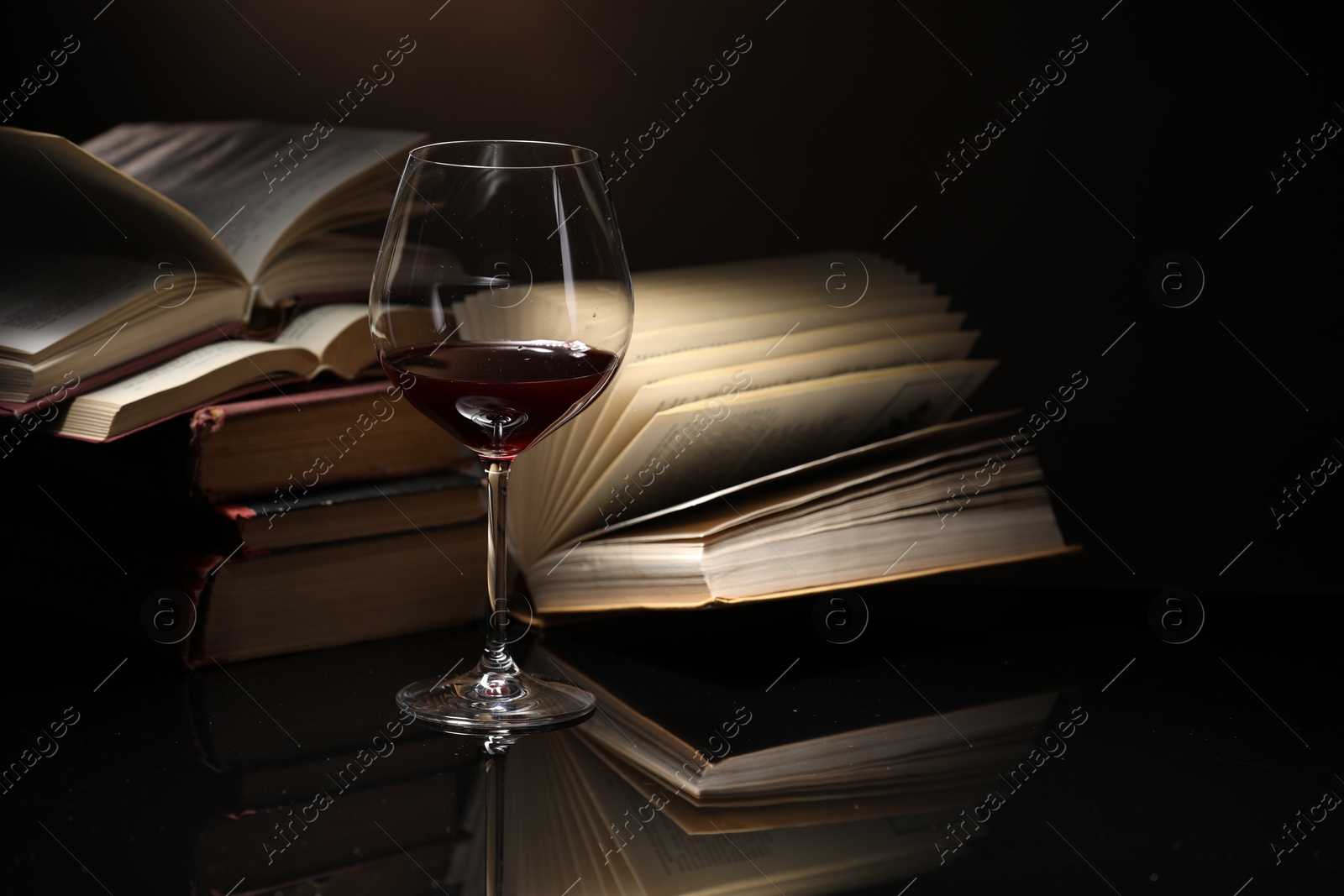 Red wine in glass and stack of books on mirror table against dark background, closeup Photo of Red wine in glass and stack of books on mirror table against dark background, closeup
