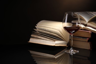 Photo of Red wine in glass and stack of books on mirror table against dark background, closeup