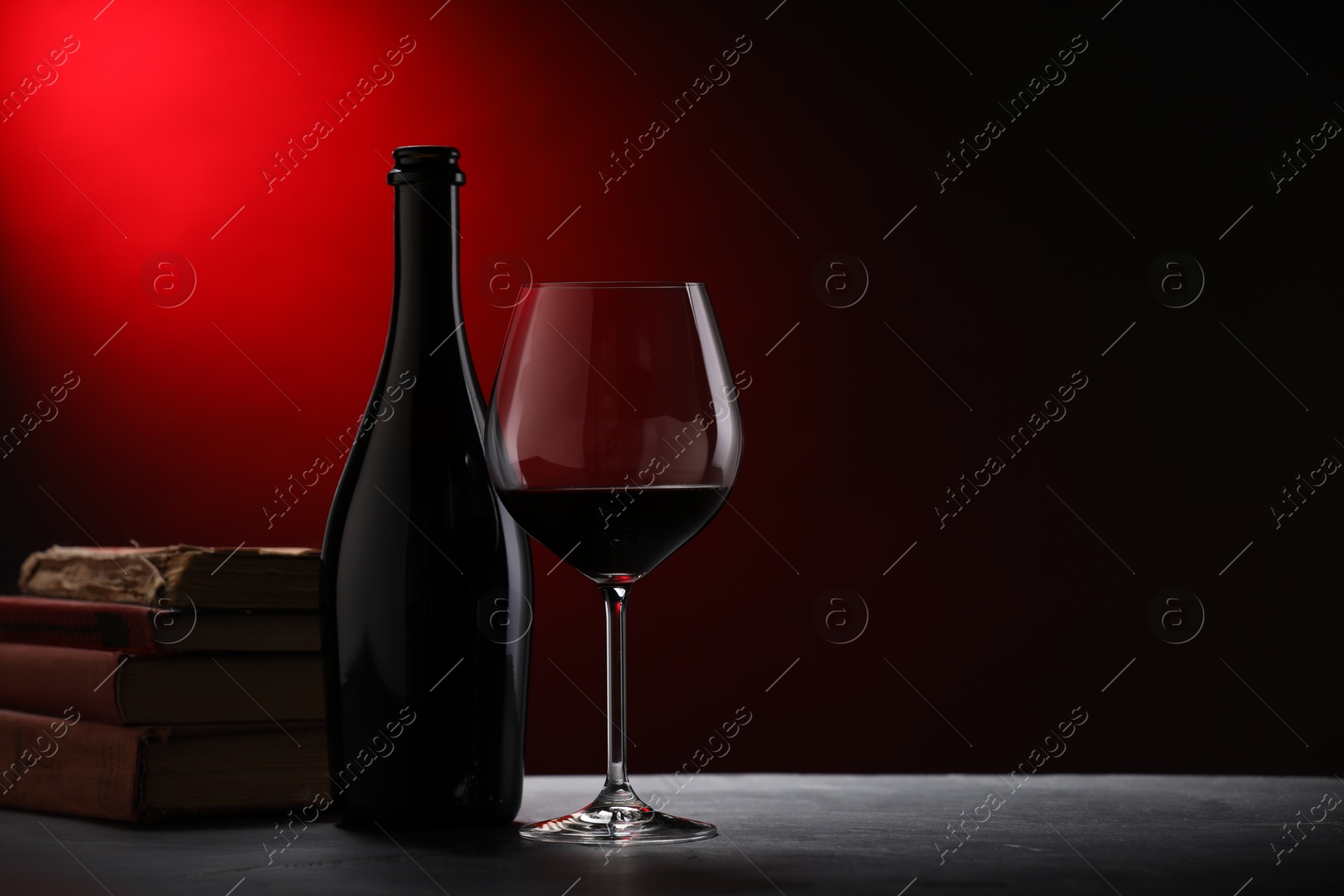Photo of Tasty wine and stacked books on dark textured table in red light, closeup