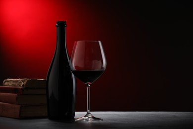 Photo of Tasty wine and stacked books on dark textured table in red light, closeup