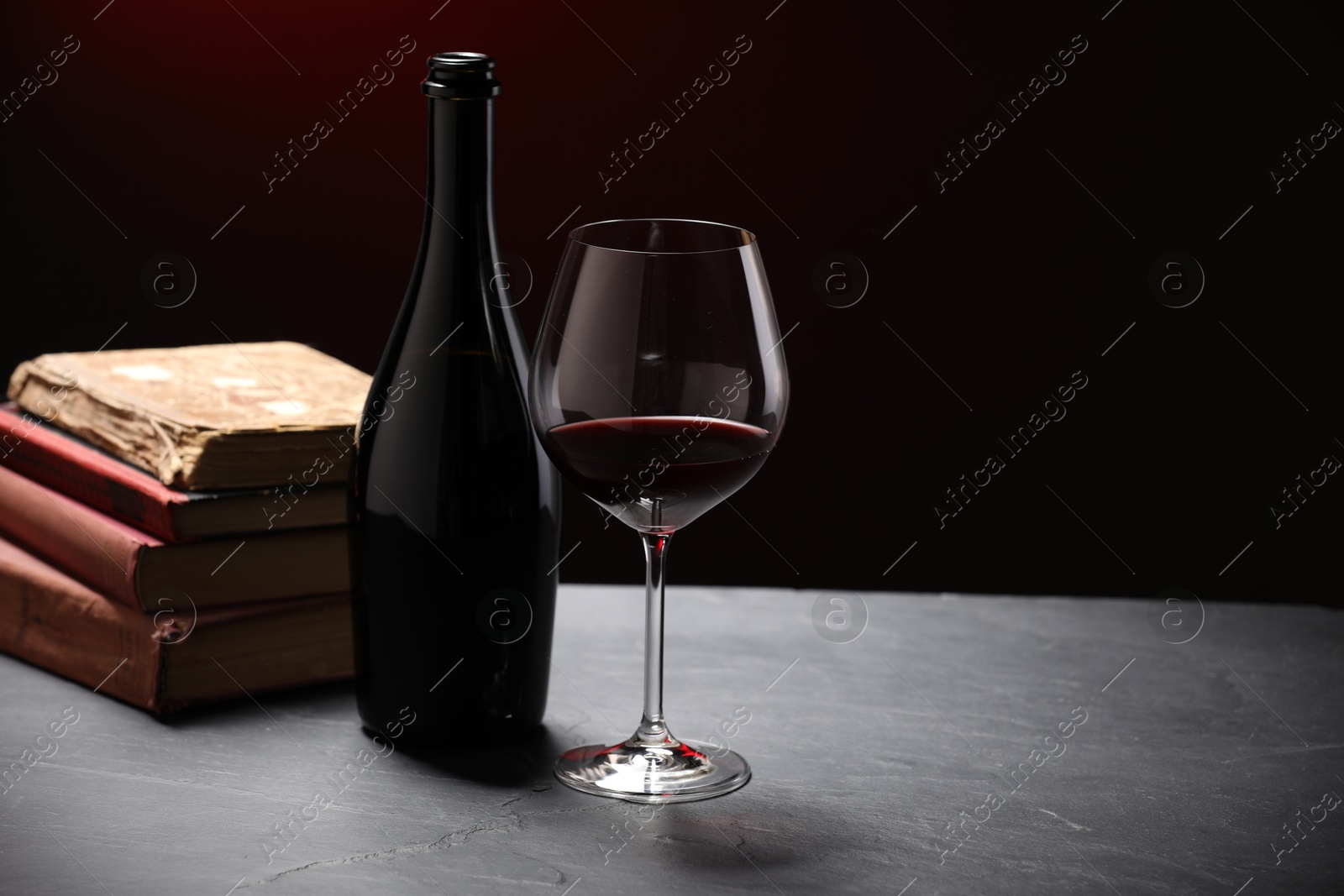 Red wine and stacked books on grey textured table against black background, closeup Photo of Red wine and stacked books on grey textured table against black background, closeup