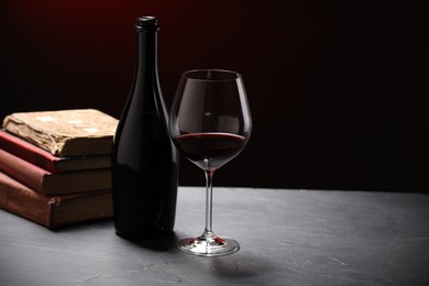 Photo of Red wine and stacked books on grey textured table against black background, closeup