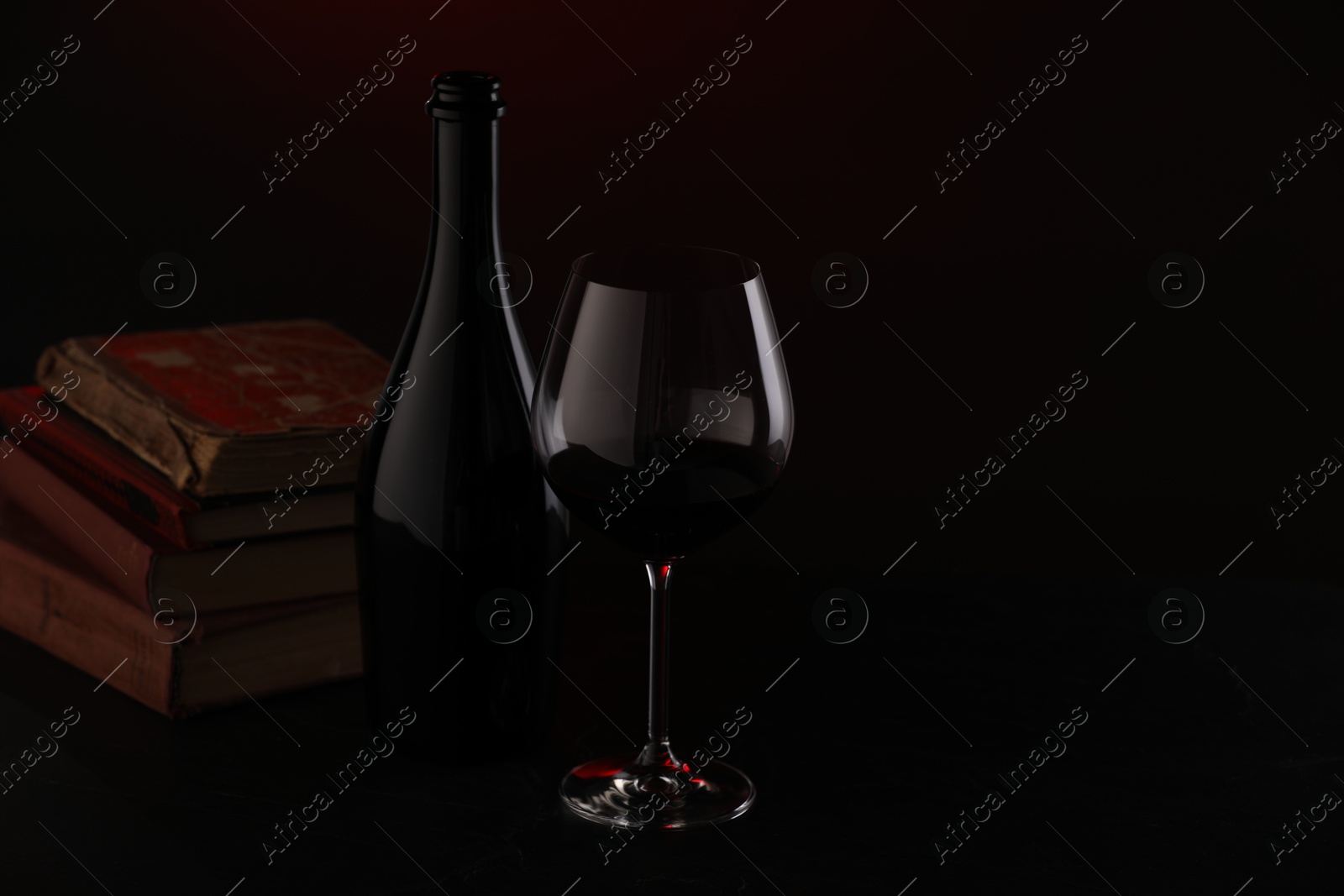 Tasty wine and stacked books in darkness, closeup Photo of Tasty wine and stacked books in darkness, closeup