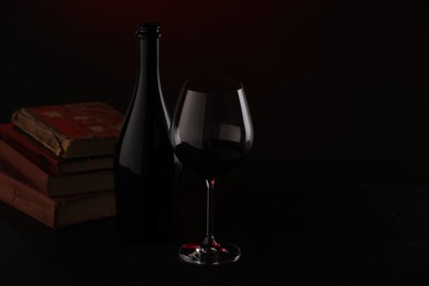 Photo of Tasty wine and stacked books in darkness, closeup