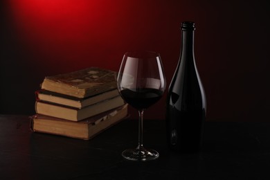 Photo of Tasty wine and stacked books on dark table in red light, closeup