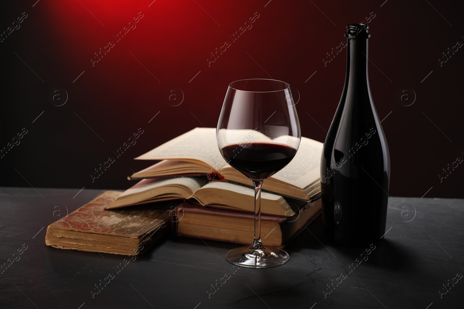 Tasty wine and stacked books on dark table in red light, closeup Photo of Tasty wine and stacked books on dark table in red light, closeup