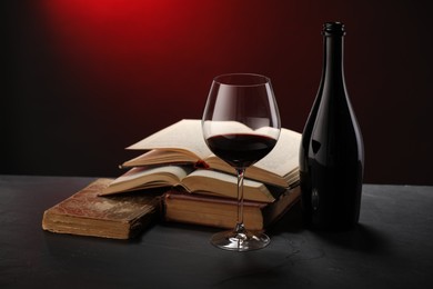 Photo of Tasty wine and stacked books on dark table in red light, closeup