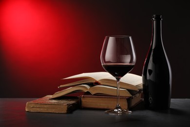 Photo of Tasty wine and stacked books on dark table in red light, closeup