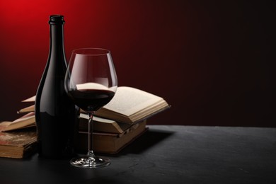 Photo of Tasty wine and stacked books on dark textured table in red light, closeup. Space for text