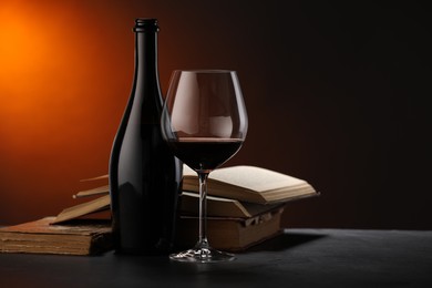 Photo of Tasty wine and stacked books on dark table in red light, closeup
