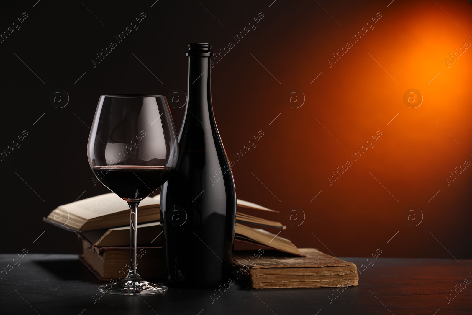 Tasty wine and stacked books on dark table in red light, closeup. Space for text Photo of Tasty wine and stacked books on dark table in red light, closeup. Space for text