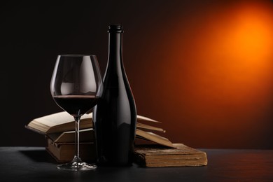 Photo of Tasty wine and stacked books on dark table in red light, closeup. Space for text