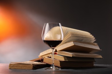Photo of Glass of tasty wine and books on dark textured table in color lights, closeup