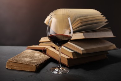 Photo of Glass of tasty wine and books on dark textured table, closeup