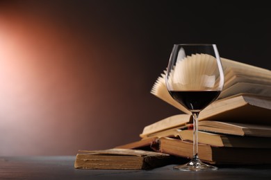 Photo of Glass of tasty wine and books on dark textured table in color lights, closeup. Space for text
