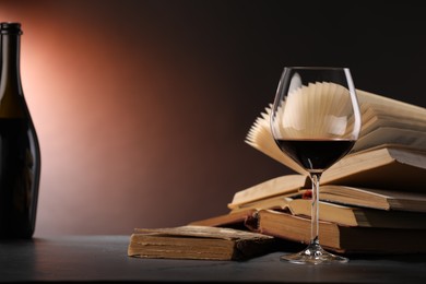 Photo of Red wine and books on dark textured table in color lights, closeup. Space for text
