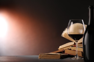 Photo of Red wine and books on dark textured table in color lights, closeup. Space for text