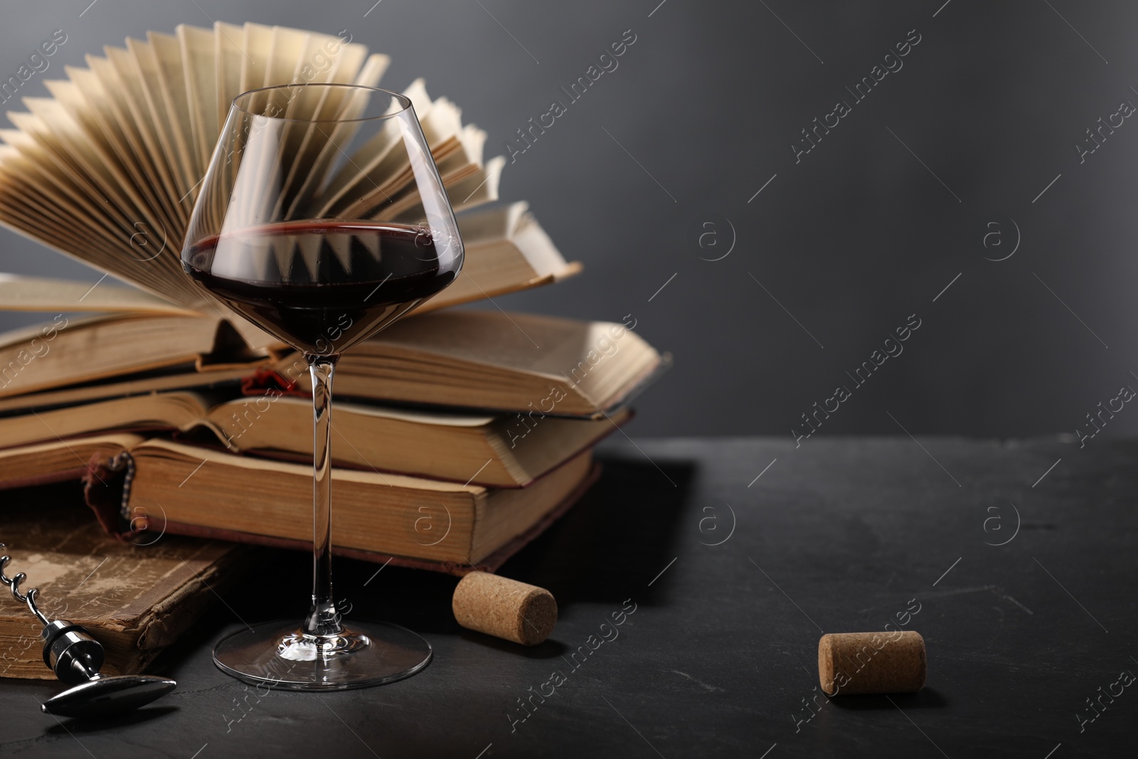 Red wine in glass and books on dark textured table against grey background, closeup. Space for text Photo of Red wine in glass and books on dark textured table against grey background, closeup. Space for text