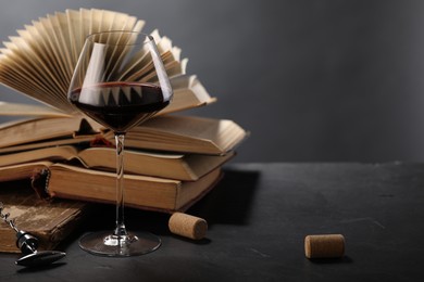 Photo of Red wine in glass and books on dark textured table against grey background, closeup. Space for text