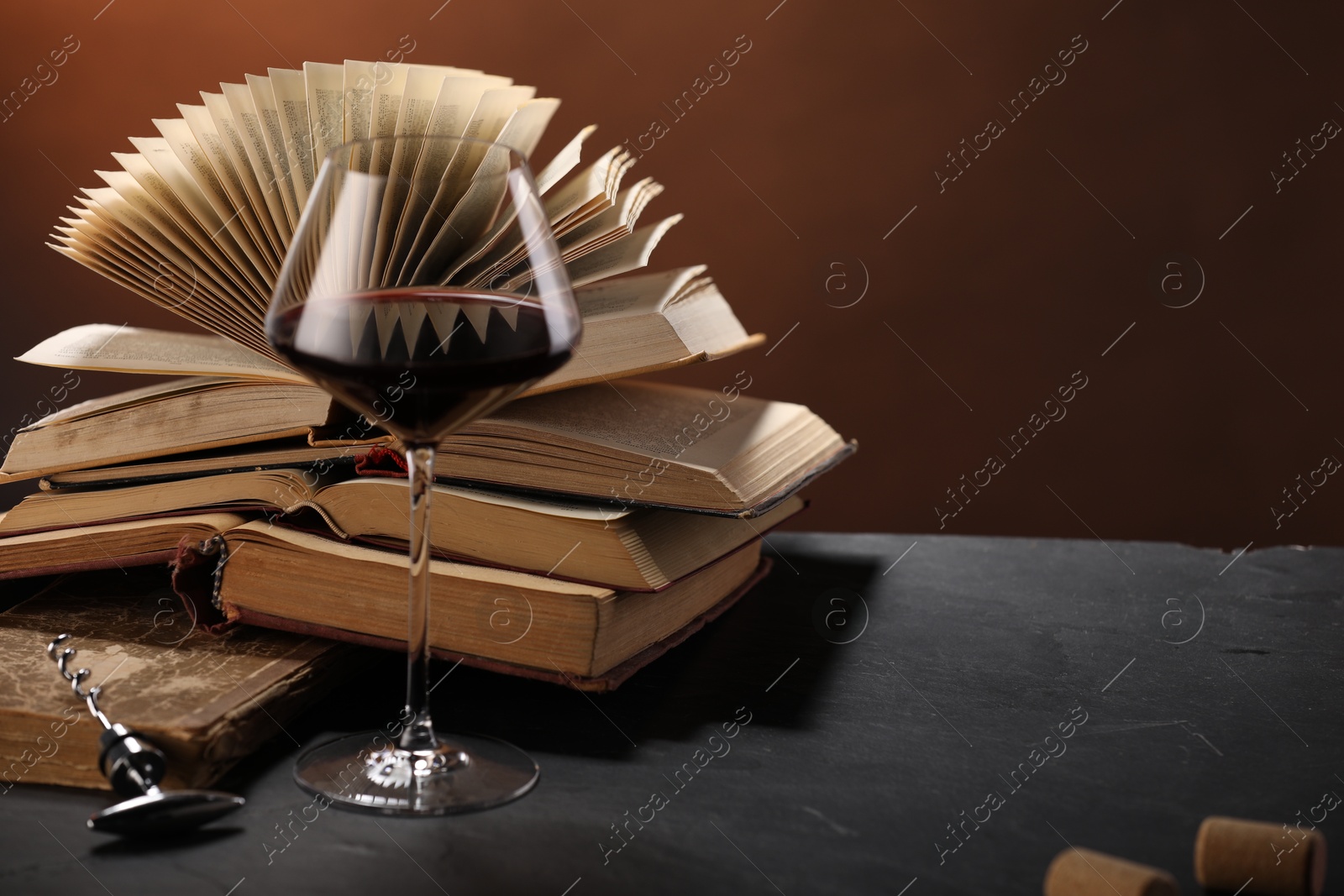 Red wine in glass and books on dark textured table against brown background, closeup. Space for text Photo of Red wine in glass and books on dark textured table against brown background, closeup. Space for text