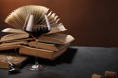 Photo of Red wine in glass and books on dark textured table against brown background, closeup. Space for text