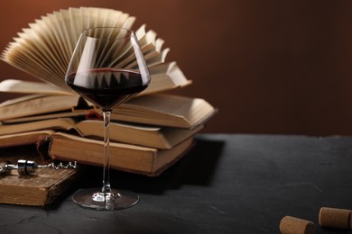 Photo of Red wine in glass and books on dark textured table against brown background, closeup. Space for text