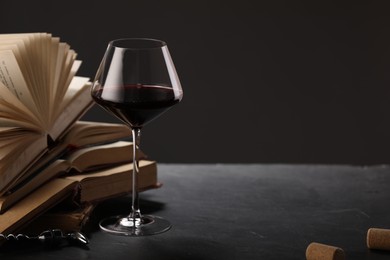 Photo of Red wine in glass and books on grey textured table against dark background, closeup. Space for text