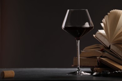 Photo of Red wine in glass and books on grey textured table against dark background, closeup. Space for text