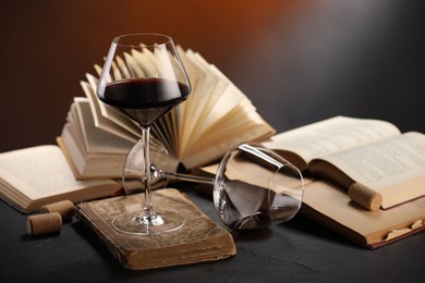 Photo of Red wine and books on dark textured table in color lights, closeup