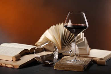 Photo of Red wine and books on dark textured table in color lights, closeup