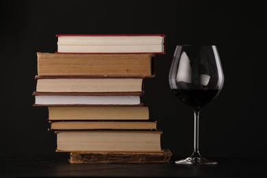 Photo of Red wine in glass and stack of books on table against black background, closeup