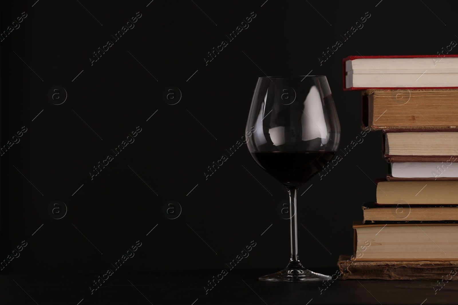 Red wine in glass and stack of books on table against black background, closeup. Space for text Photo of Red wine in glass and stack of books on table against black background, closeup. Space for text