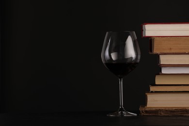 Photo of Red wine in glass and stack of books on table against black background, closeup. Space for text