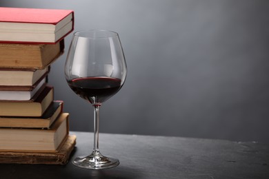 Photo of Red wine in glass and stack of books on grey textured table, closeup. Space for text