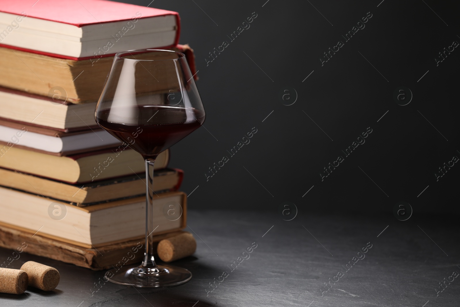 Red wine in glass and stack of books on grey textured table against dark background, closeup. Space for text Photo of Red wine in glass and stack of books on grey textured table against dark background, closeup. Space for text