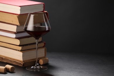 Photo of Red wine in glass and stack of books on grey textured table against dark background, closeup. Space for text