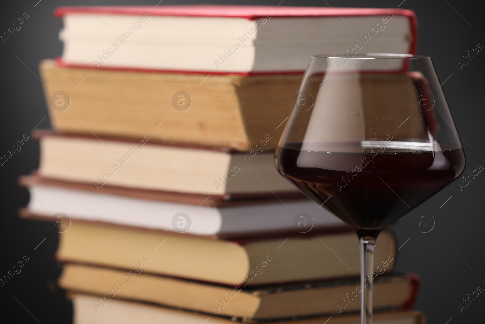 Red wine in glass and stack of books on dark background, closeup Photo of Red wine in glass and stack of books on dark background, closeup