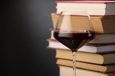 Photo of Red wine in glass and stack of books on dark background, closeup. Space for text