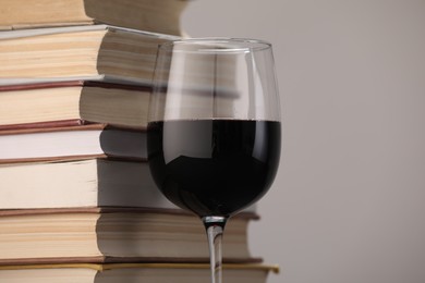 Photo of Red wine in glass and stack of books on light grey background, closeup. Space for text