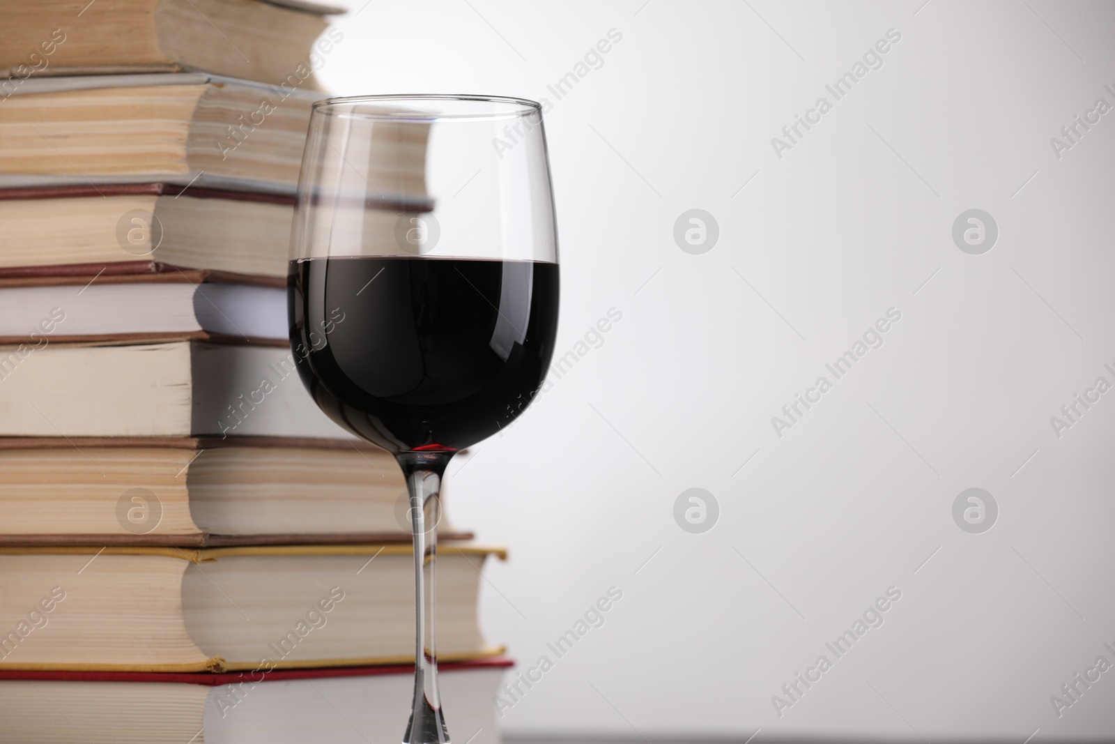 Red wine in glass and stack of books on light background, closeup. Space for text Photo of Red wine in glass and stack of books on light background, closeup. Space for text