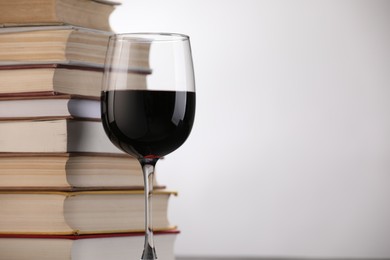Photo of Red wine in glass and stack of books on light background, closeup. Space for text