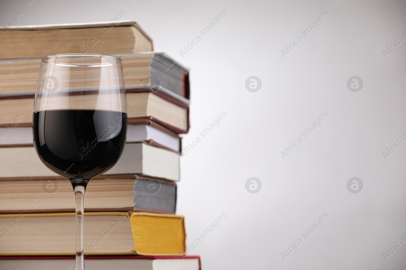 Red wine in glass and stack of books on light background, closeup. Space for text Photo of Red wine in glass and stack of books on light background, closeup. Space for text