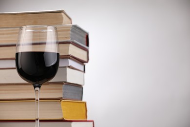 Photo of Red wine in glass and stack of books on light background, closeup. Space for text