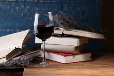 Photo of Red wine in glass, lavender flowers and books on wooden table against blue background, closeup