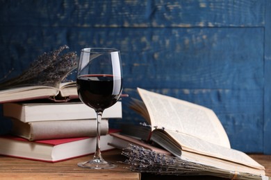 Photo of Red wine in glass, lavender flowers and books on wooden table against blue background, closeup