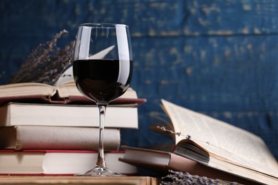 Photo of Red wine in glass, lavender flowers and books against blue wooden background, closeup